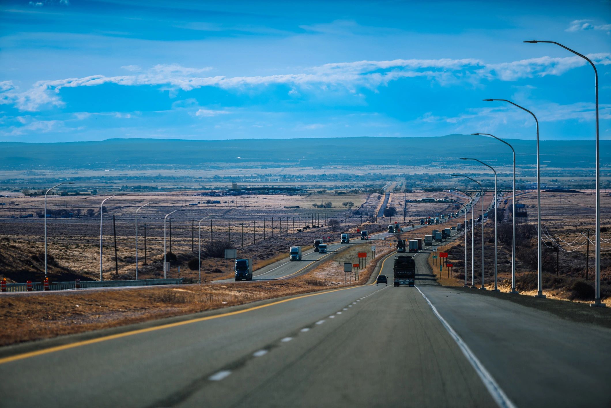 Highway through a western landscape with trucks and mountains in the distance.